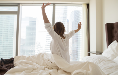 Kvinde sidder i sengen og er klar til en ny dag. Kigger ud på skyskrabere.