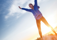 Kvinde står på en bjergtop i afslappet tøj med armene i vejret og udstråler en vinder følelse