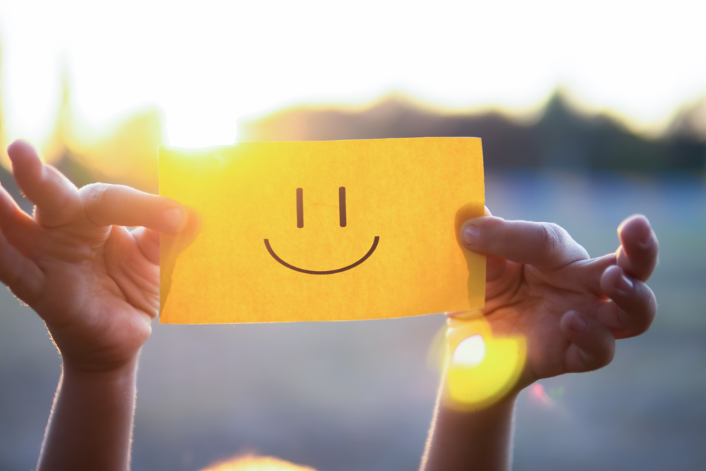 To hænder holder en post it op med en smilende mund