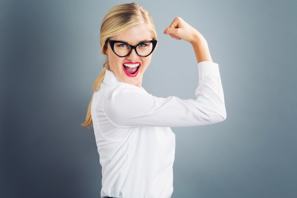 Kvinde i hvid skjorte og med sorte briller viser powerpose med højre arm.